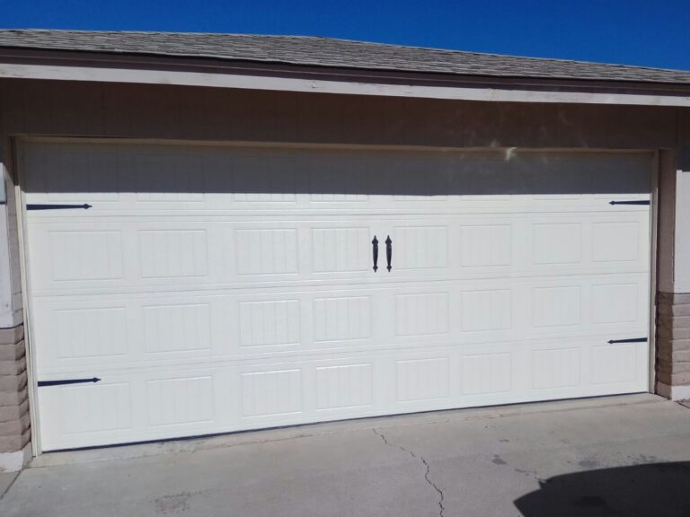 White carriage-style double garage door with black decorative hinges and handles on a single-story home